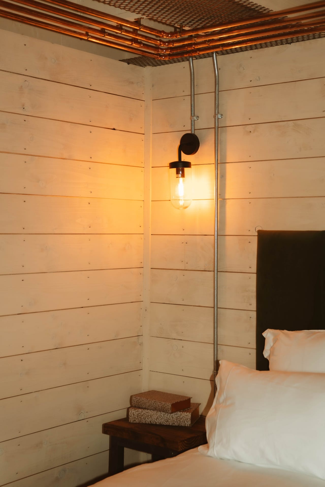 Treehouse Lookout bedside wall light beneath copper ceiling pipework