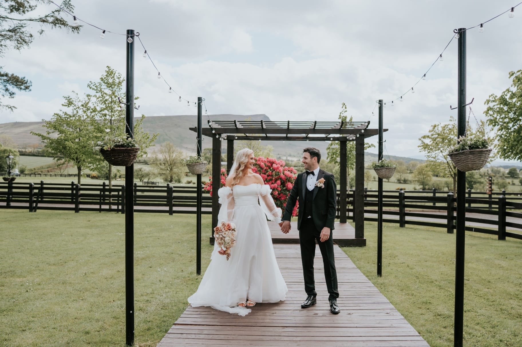 Bride and groom walking hand in hand under the garden pergola with mountain views