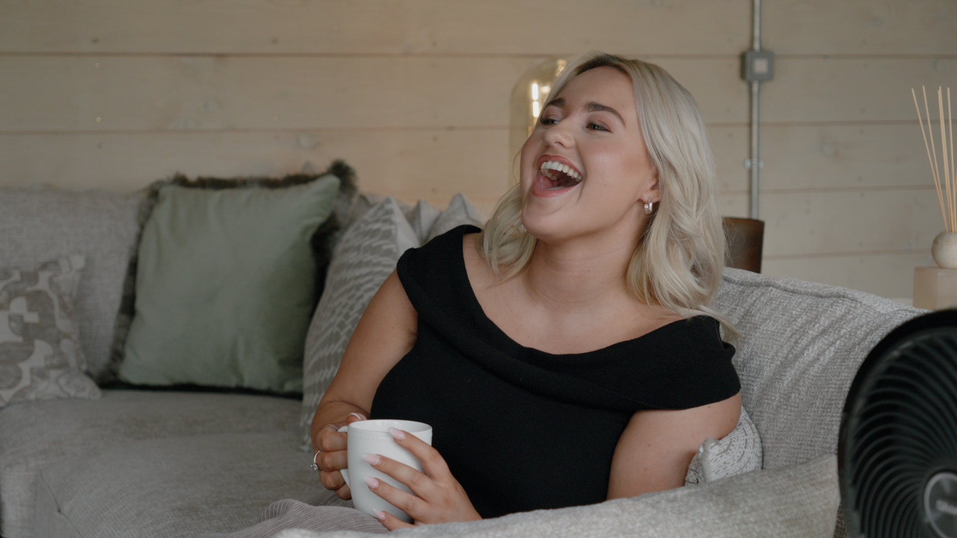 A laughing guest relaxing on the treehouse sofa with a morning mug