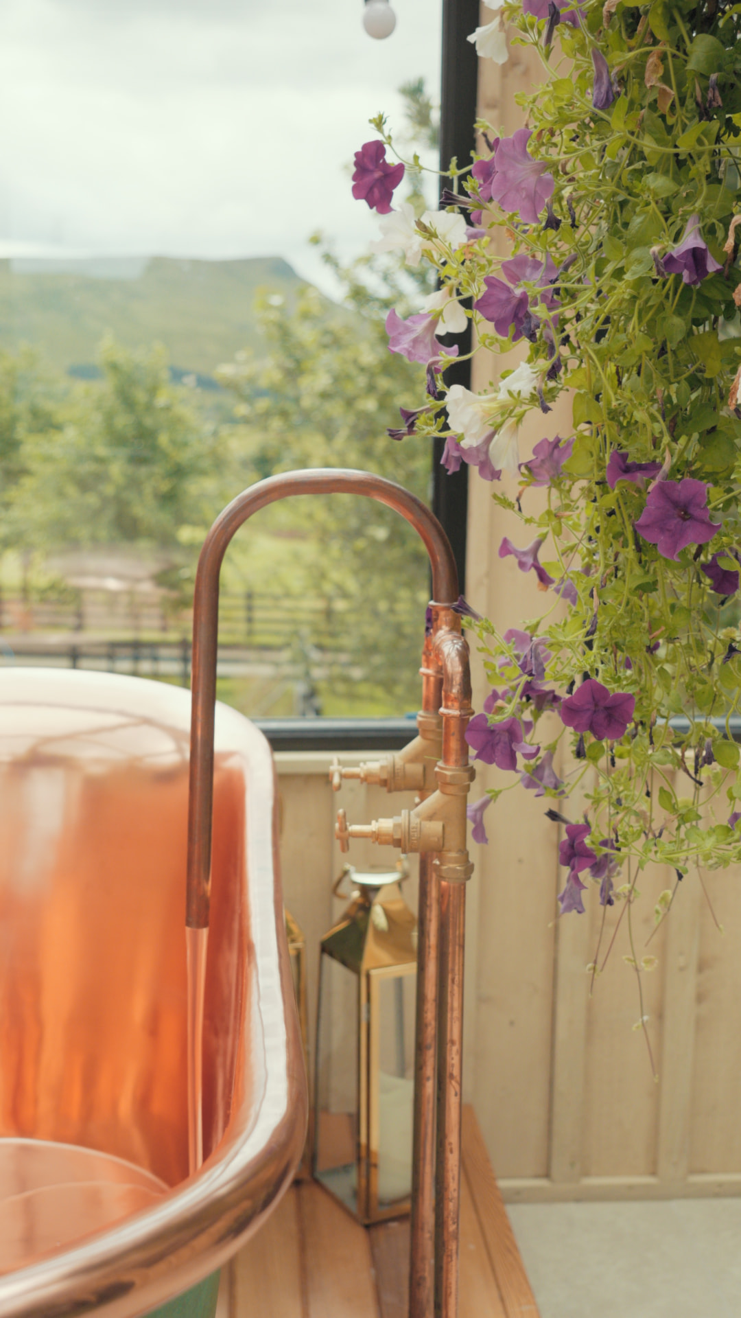 Copper bath with brass taps beside trailing purple and white flowers and views of the Ballyness countryside
