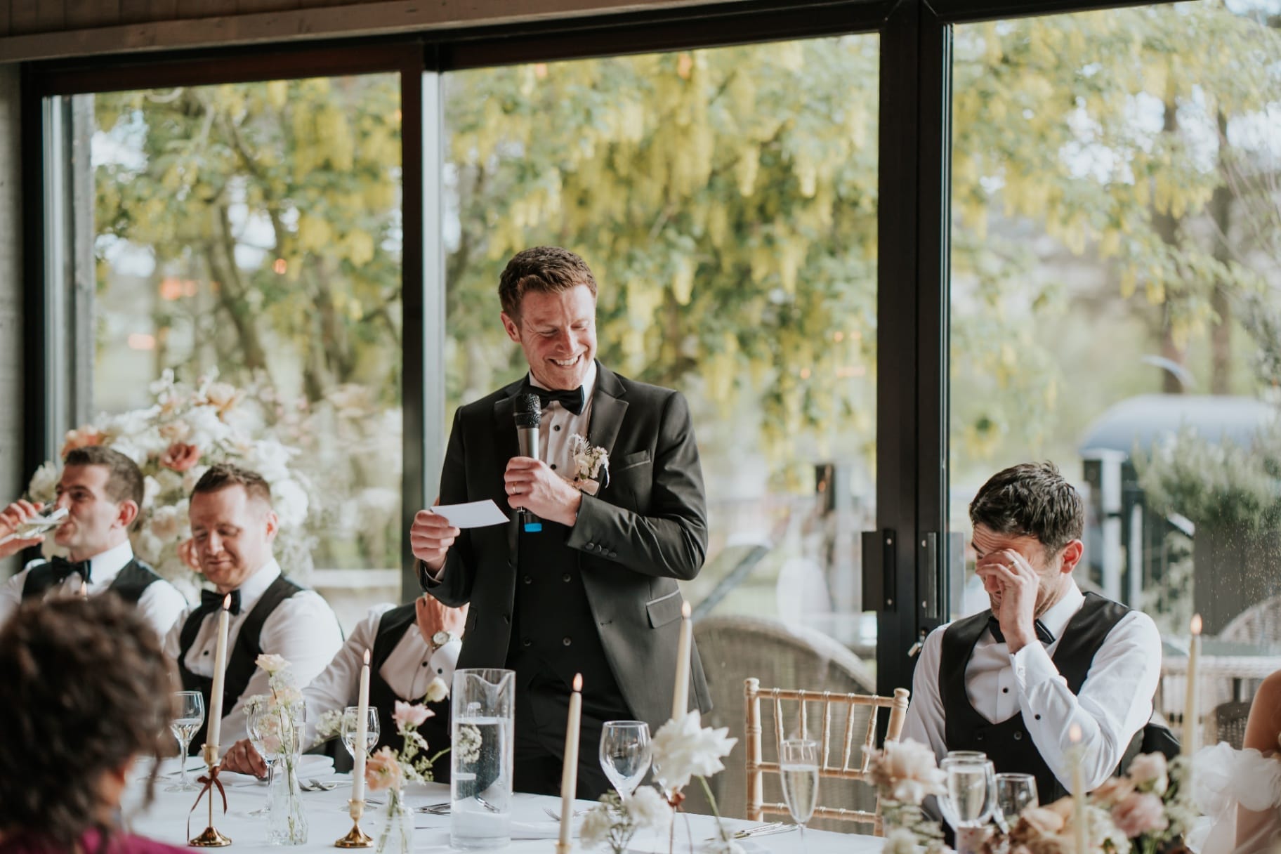 Groomsman giving a speech while another wipes away tears at the top table