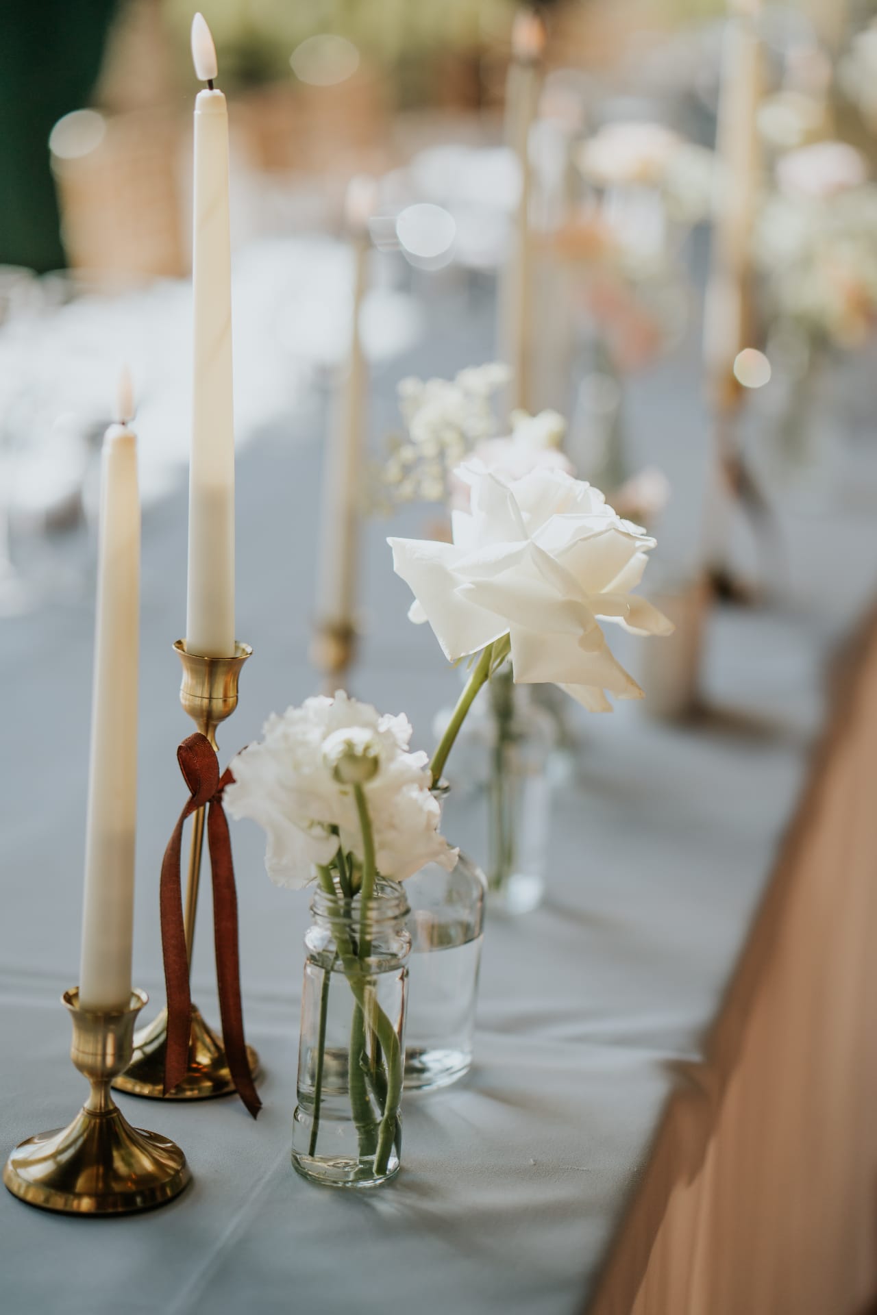 Taper candles and white roses in bud vases along the wedding table