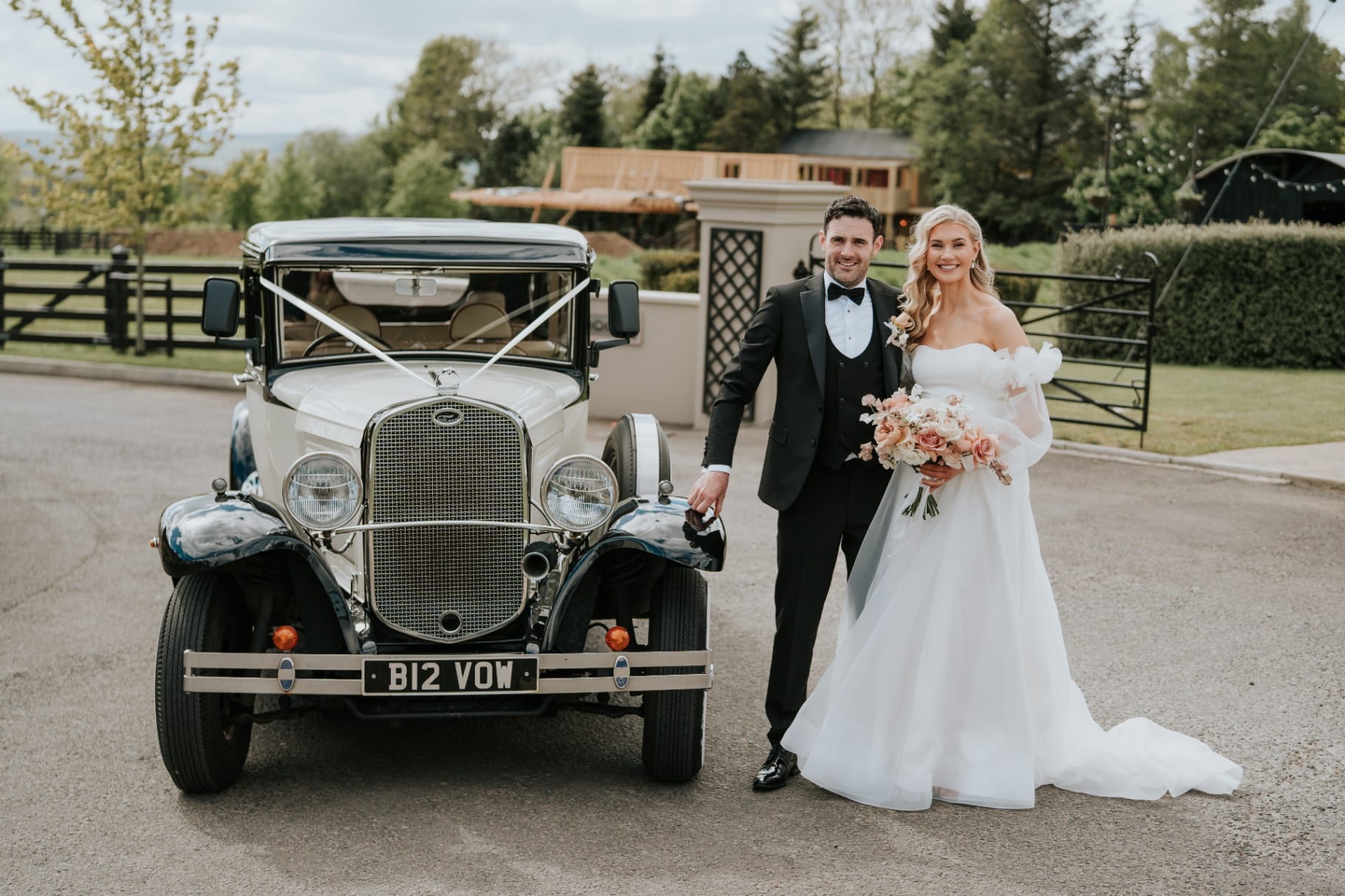 Bride and groom posing beside the vintage wedding car