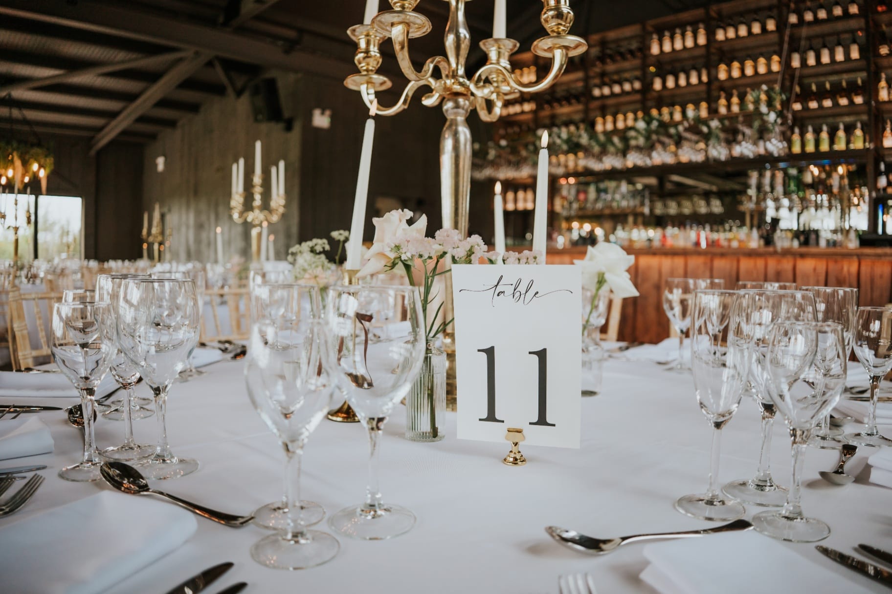 Reception tables dressed with candelabra and bar wall behind