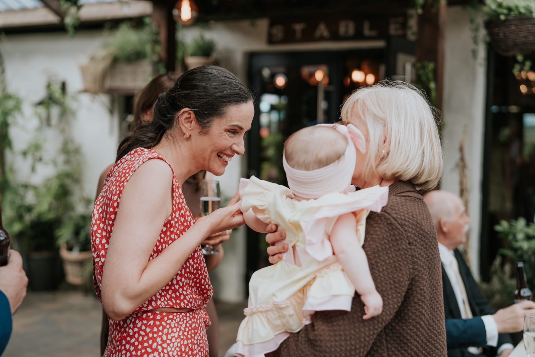 Wedding guests greeting a baby outside The Stables