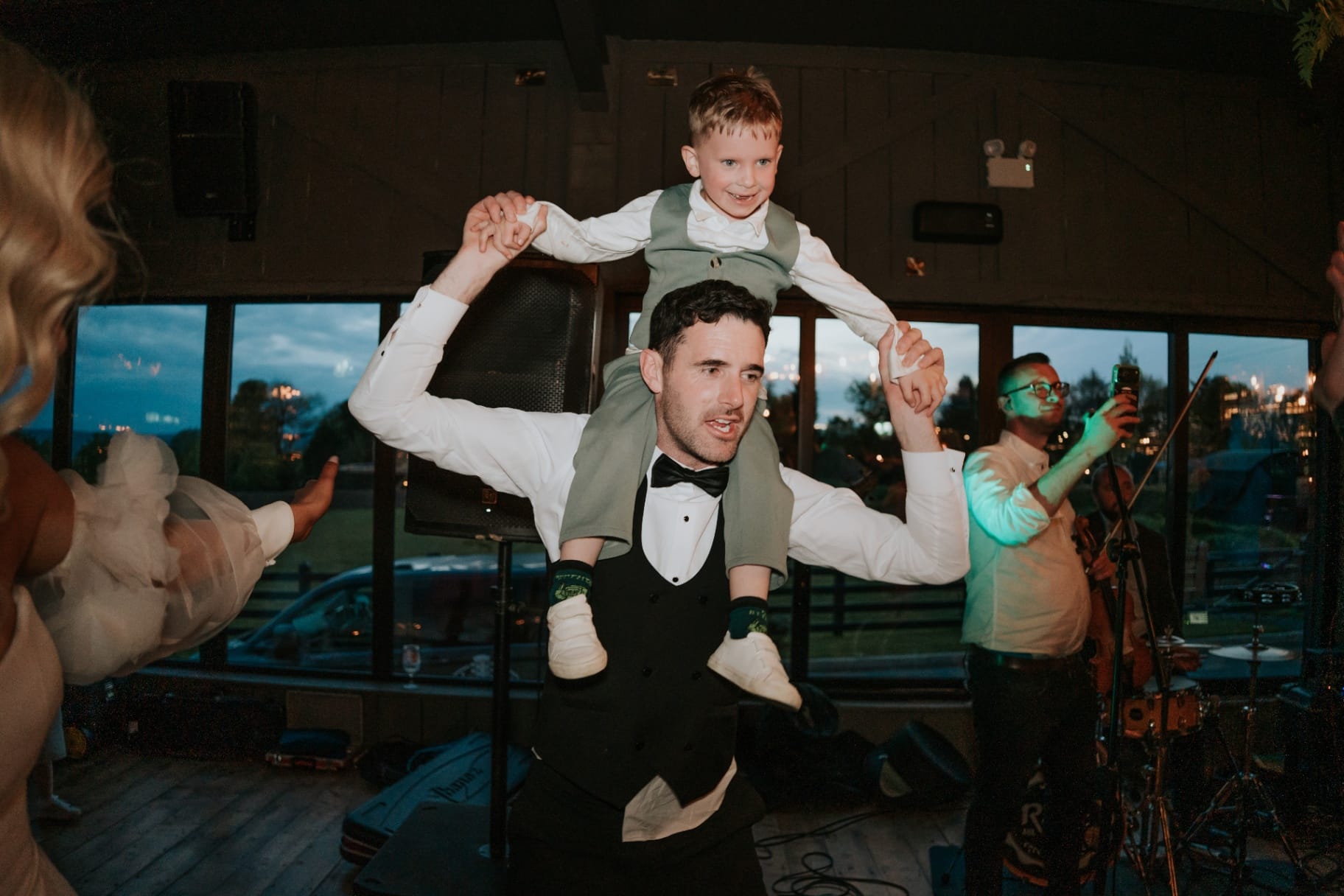 Groomsman with young page boy on his shoulders during evening celebrations