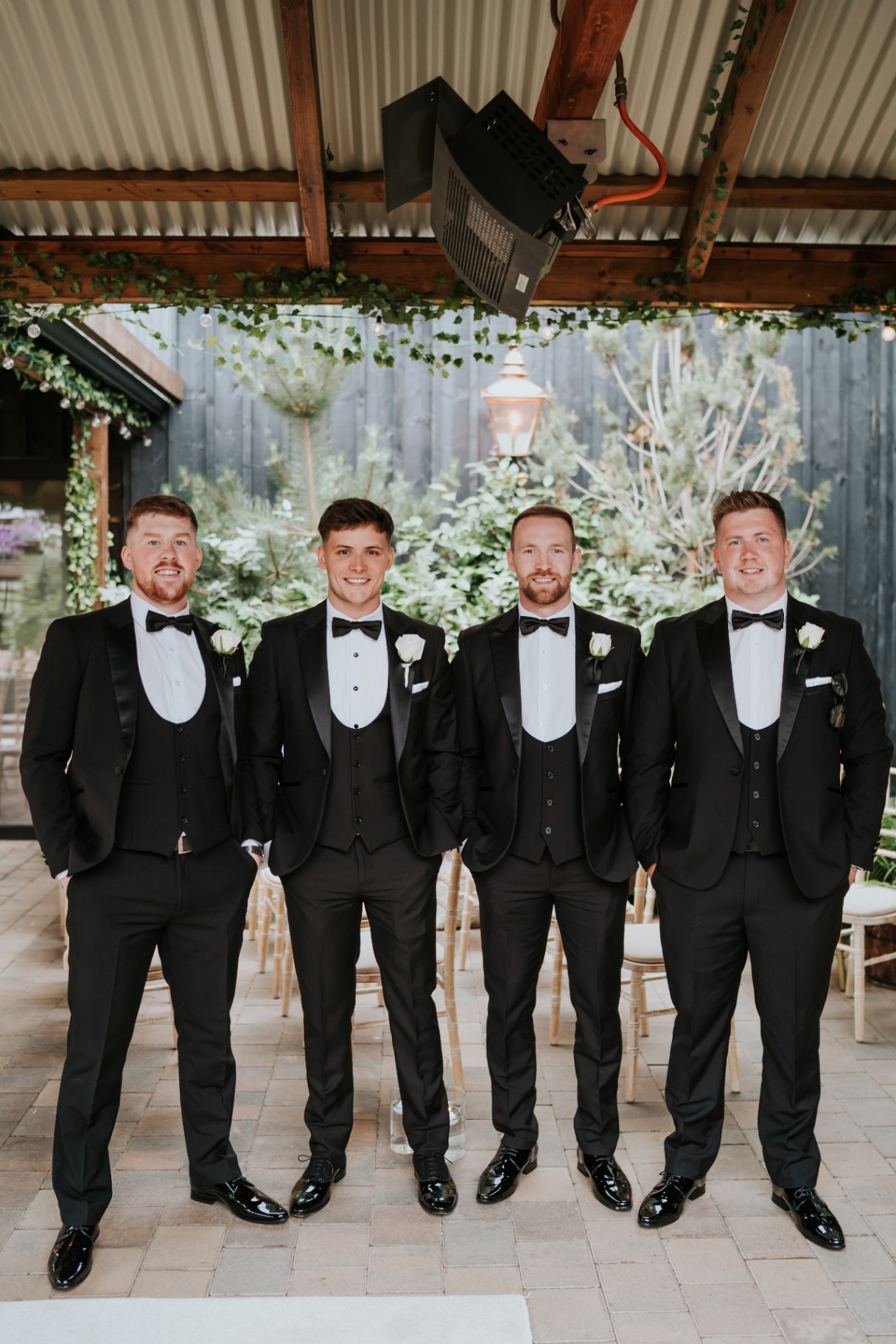 Groomsmen in black tuxedos beneath the ivy-clad pergola
