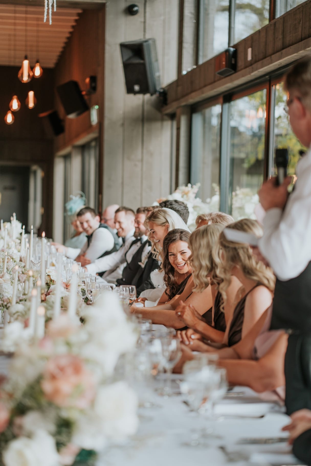 Bridal party laughing during speeches at the long candlelit top table