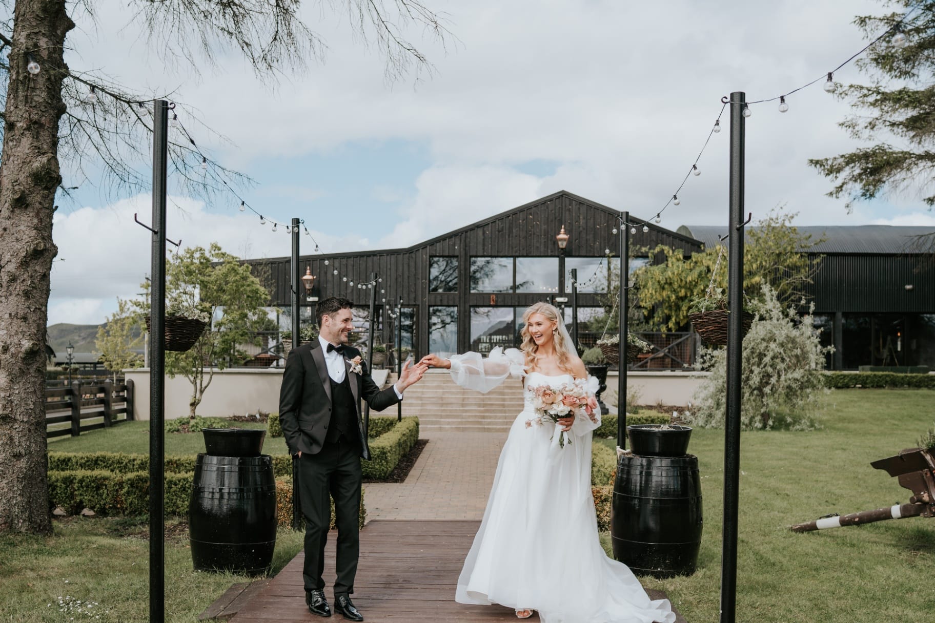 Bride and groom on the boardwalk in front of The Barn with festoon lights overhead