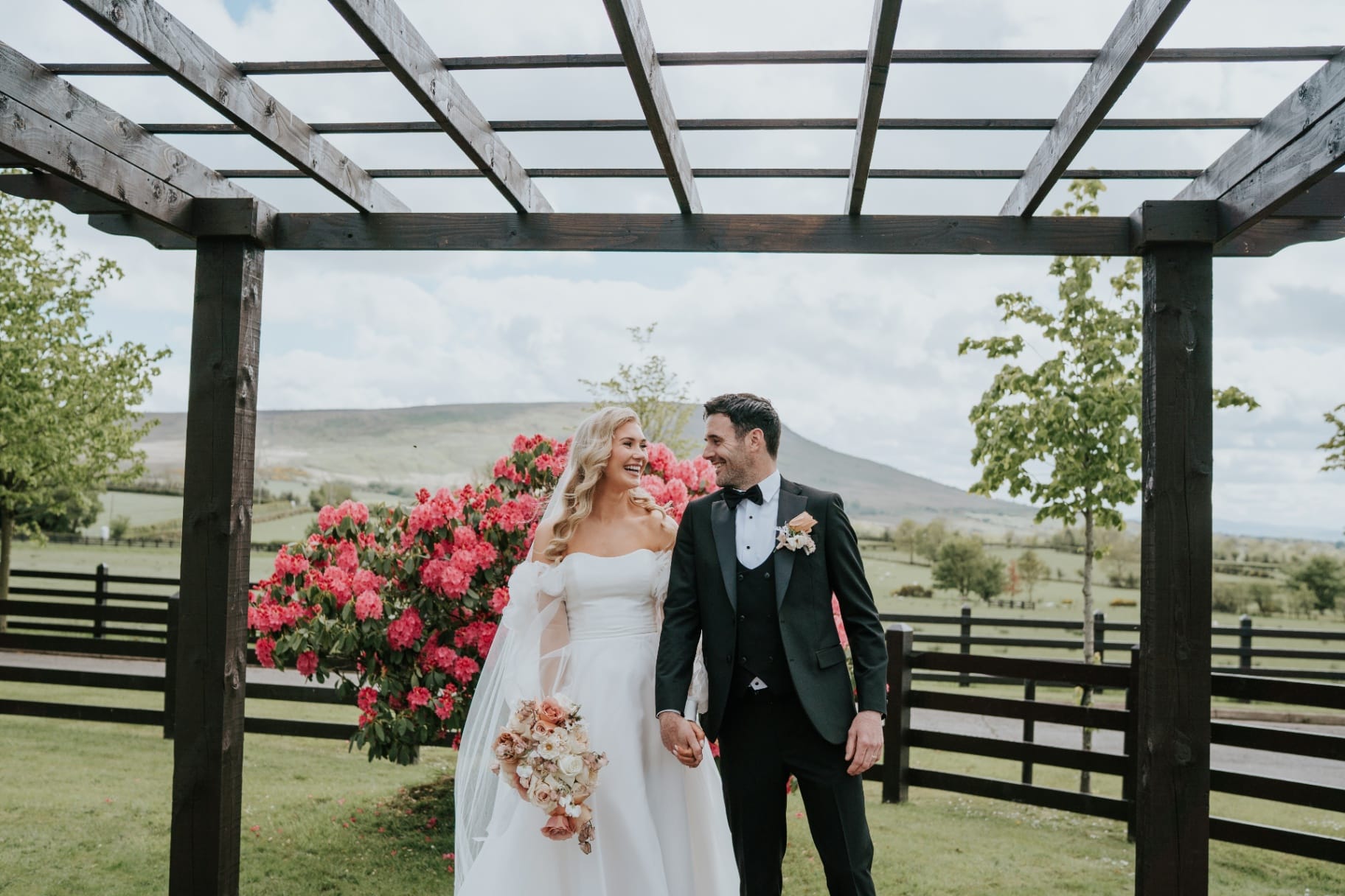 Laughing bride and groom under the pergola with rhododendrons and Benbradagh behind
