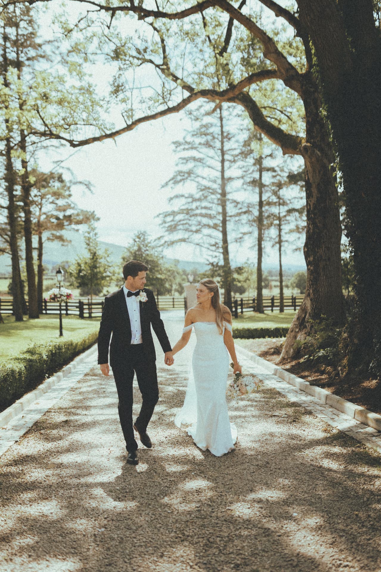 The bride and groom walking hand in hand along a tree-lined path at Ballyness Resort