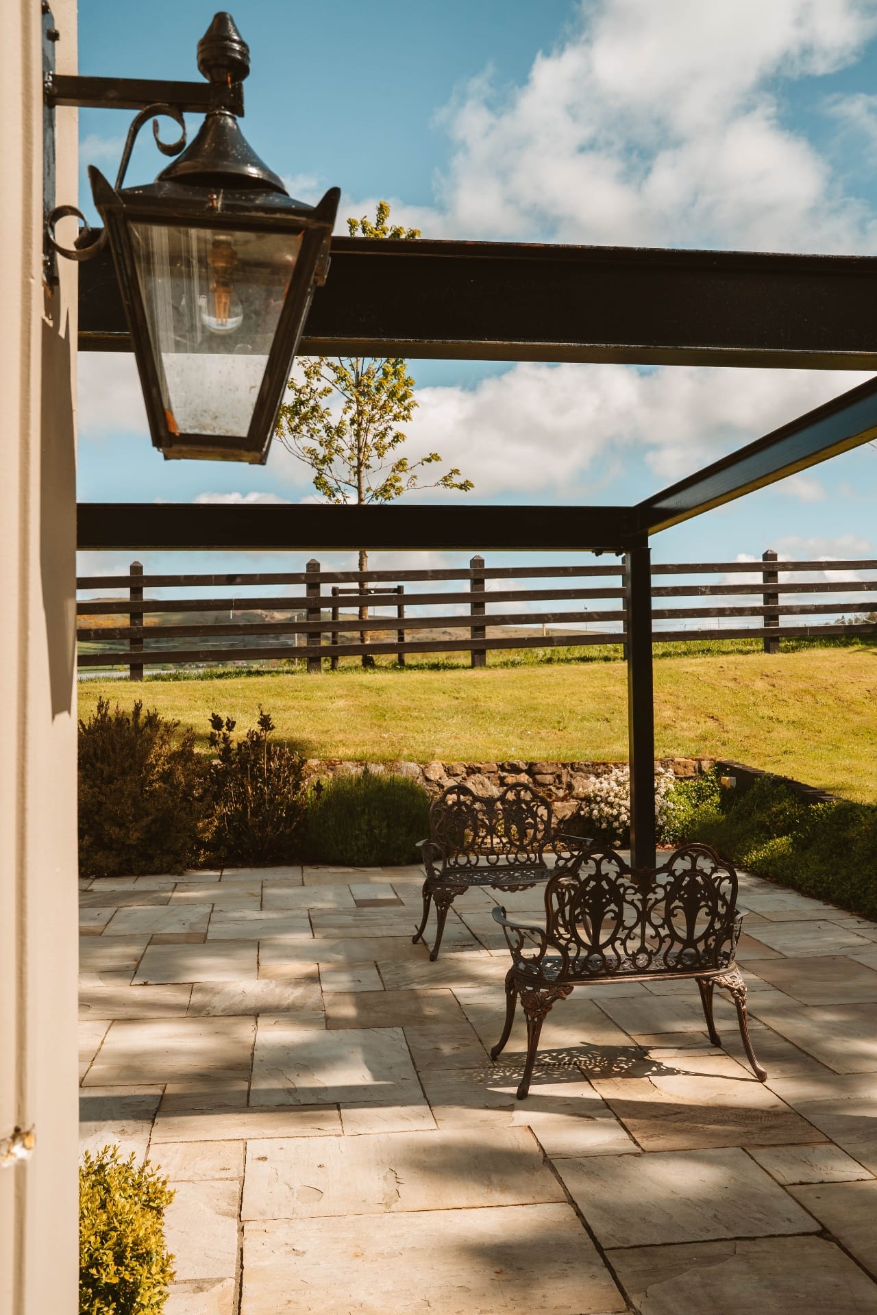 Sunlit flagstone terrace beneath the wrought-iron lantern and pergola