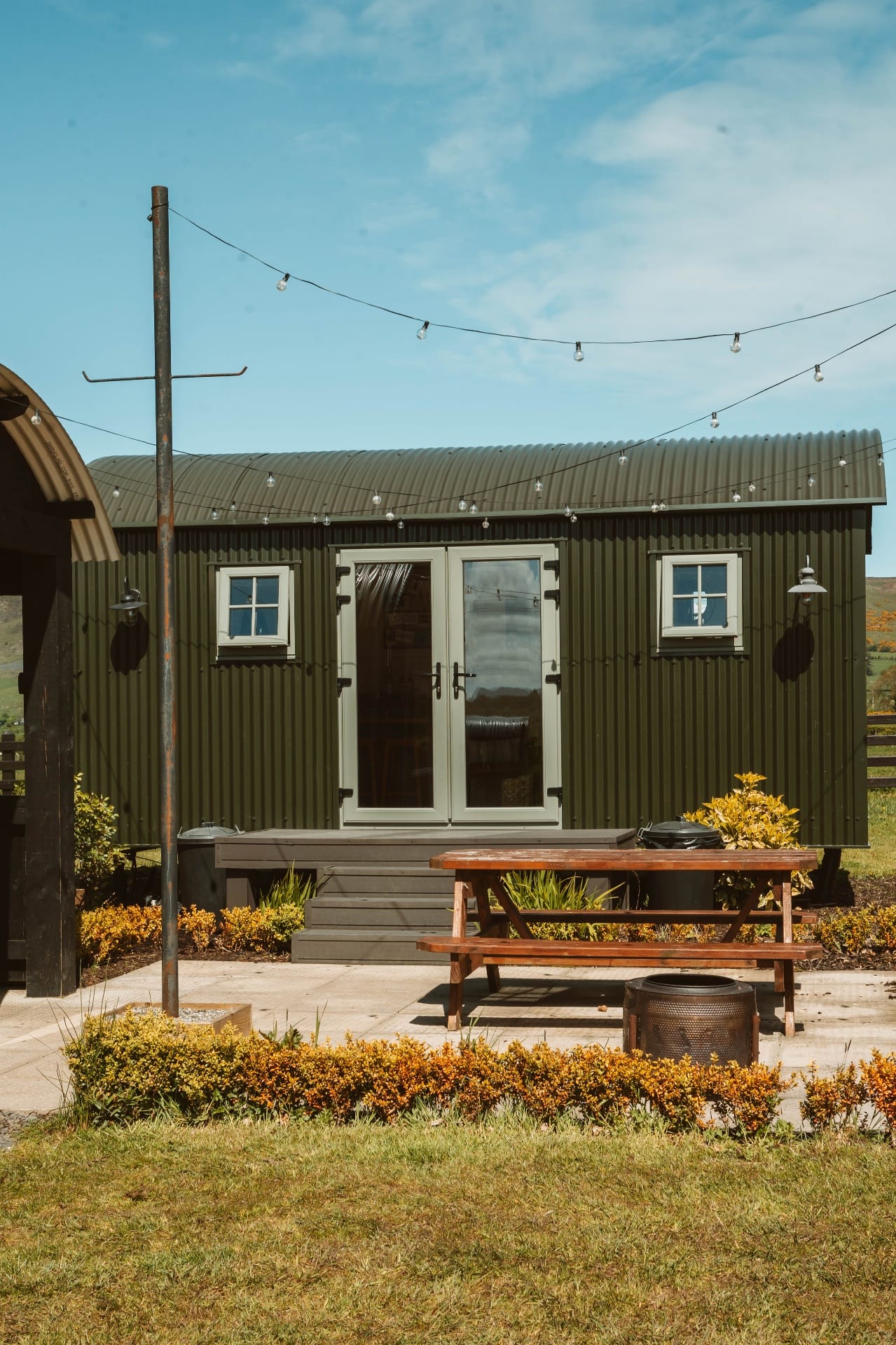 Green Shepherd's Hut exterior with picnic bench and festoon lights